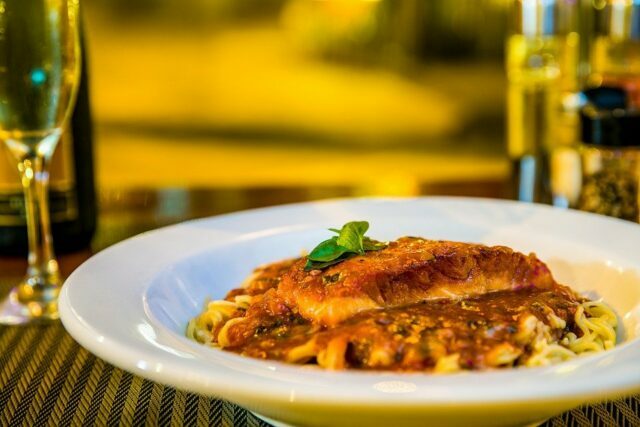 Comida italiana em um prato branco em cima de uma mesa com taça