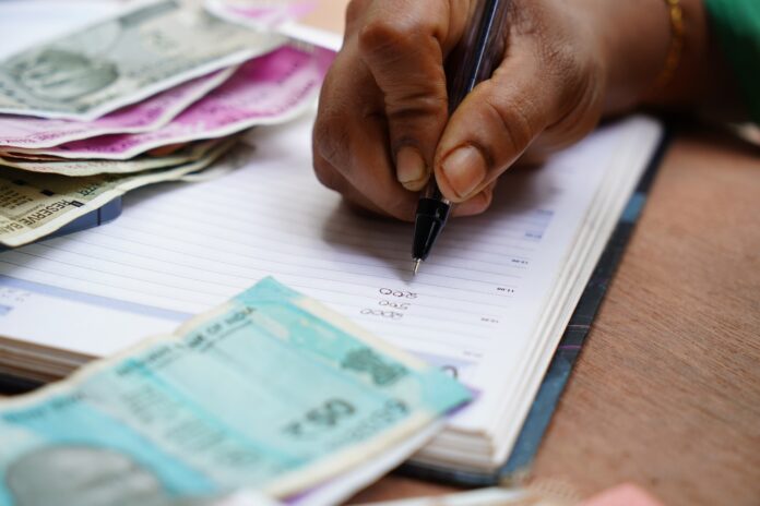 Homem fazendo cálculos em um caderno com várias notas de dinheiro