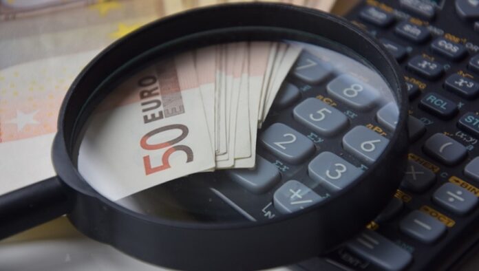 custos x despesas Lupa em cima de notas de 50 euros em cima de uma calculadora