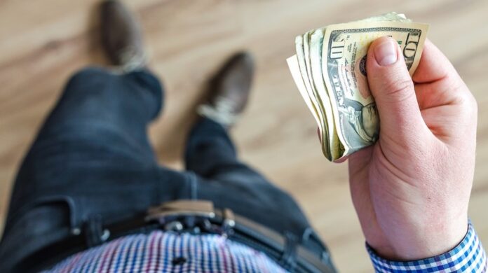 homem visto de cima segurando dólar nas mãos