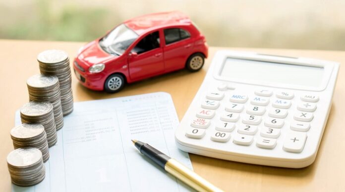 Calculadora, papeis com anotação, caneta, moedas empilhadas e um carro vermelho em miniatura
