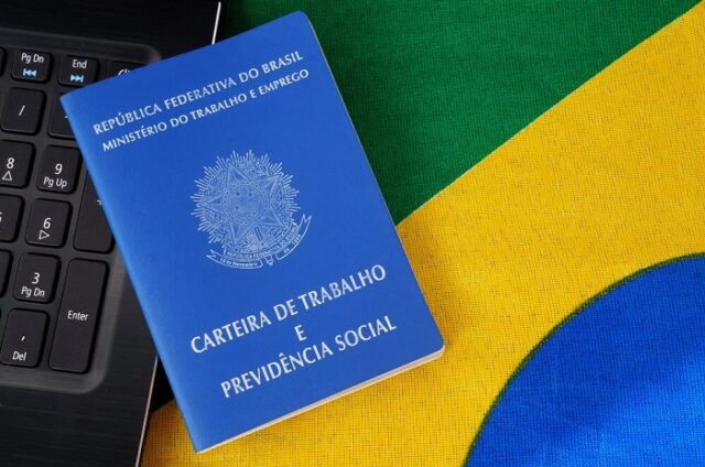 Parte de um teclado com um carteira de trabalho em cima de uma parte da bandeira do Brasil