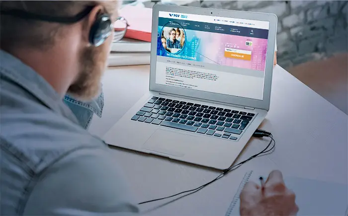 Homem de fone de ouvido acessando site da FGV em um notebook