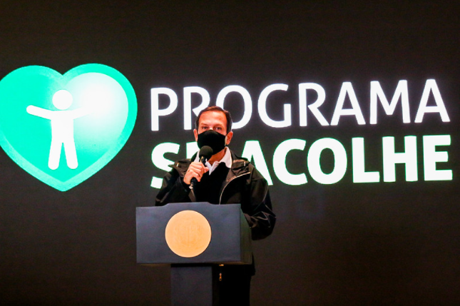 Governador João Dória de máscara preta falando no microfone