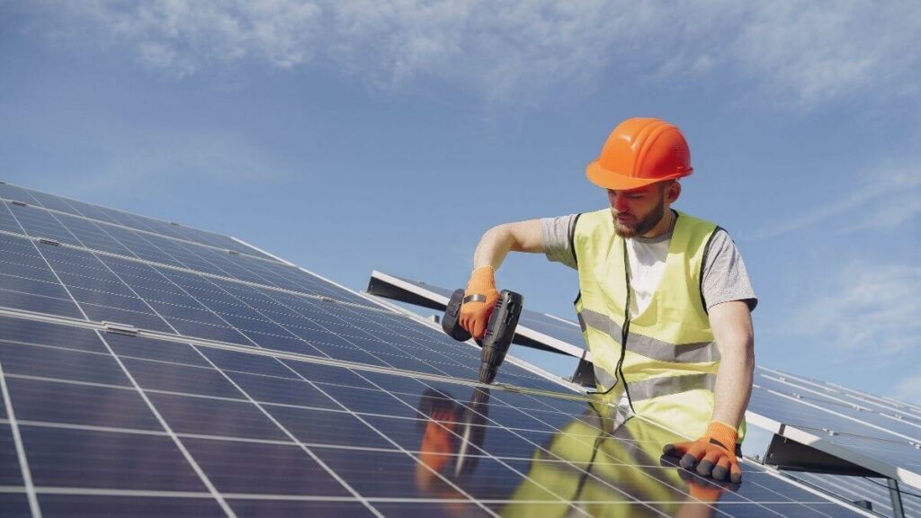 Homem com capacete de segurança parafusa um painel de energia solar em um telhado