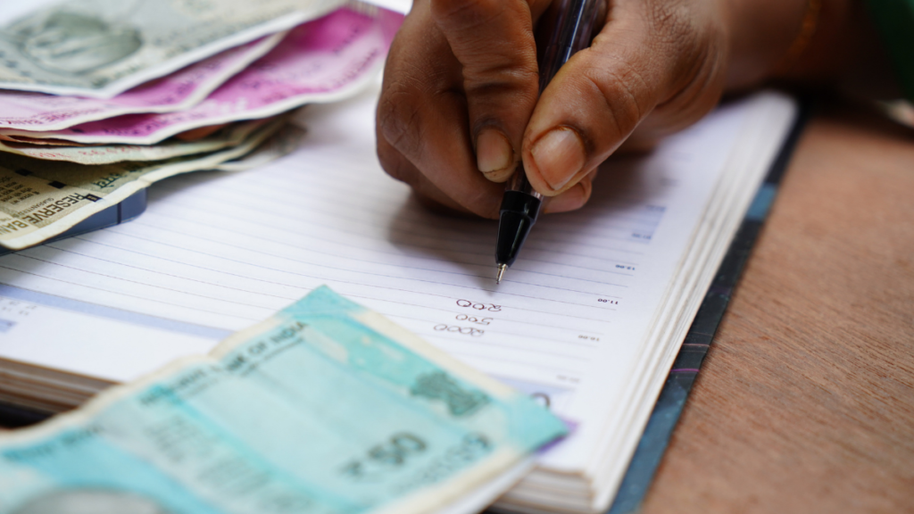 Mão masculina fazendo contas num caderno com várias notas de dinheiro em volta