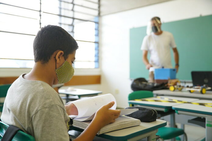 aluno em sala de aula e monitor sanitário com máscara a frente