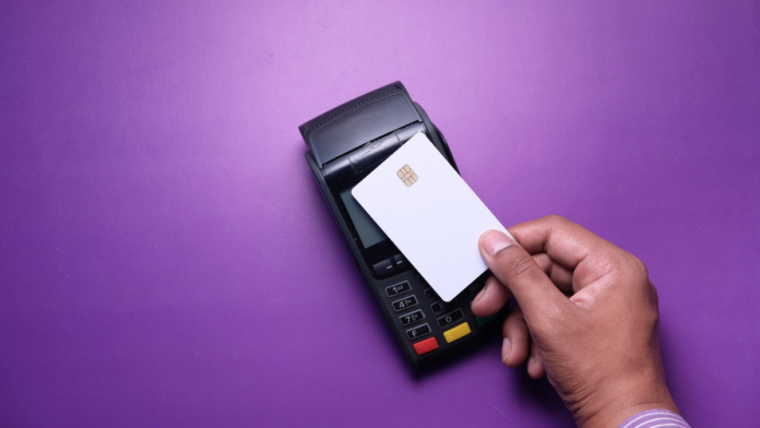 Homem segurando o cartão de aproximação Nubank com máquina de cartão em um fundo roxo