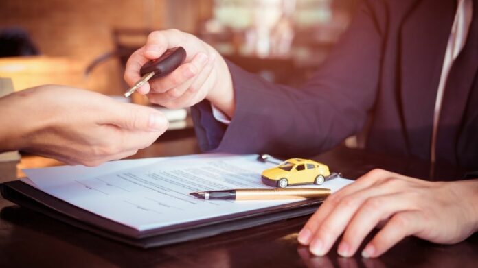 leasing Pessoa entrega chave de carro na mão de outra, com um contrato de leasing aparecendo apoiado na mesa abaixo