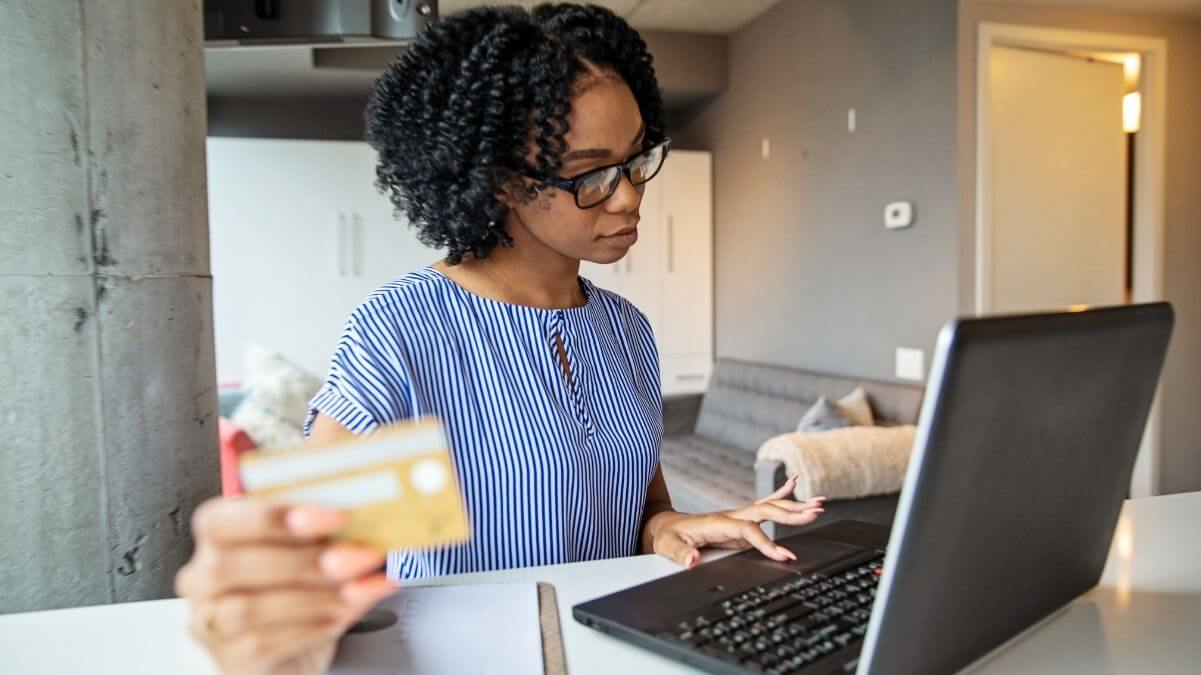 Mulher segura um cartão de crédito e digita em um notebook