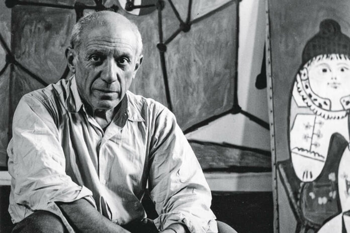 Pablo Picasso sentado em frente e uma de suas obras
