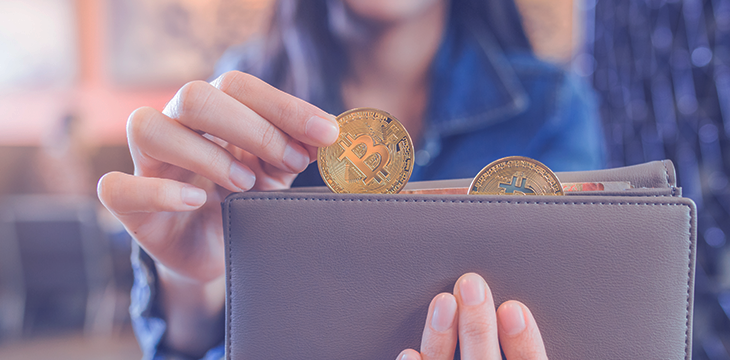 Mulher coloca moeda de Bitcoin na carteira