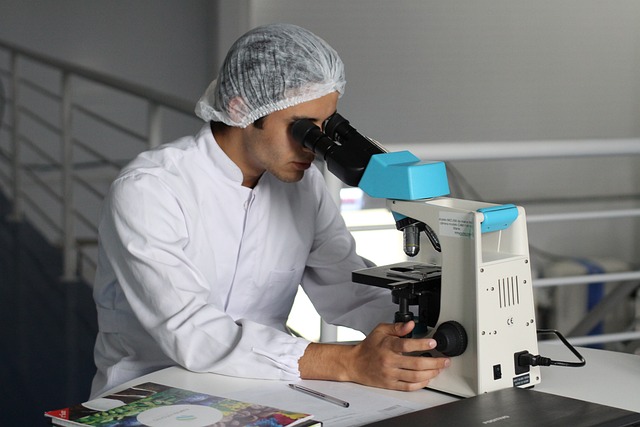 Cientista homem de jaleco olhando em um microscópio